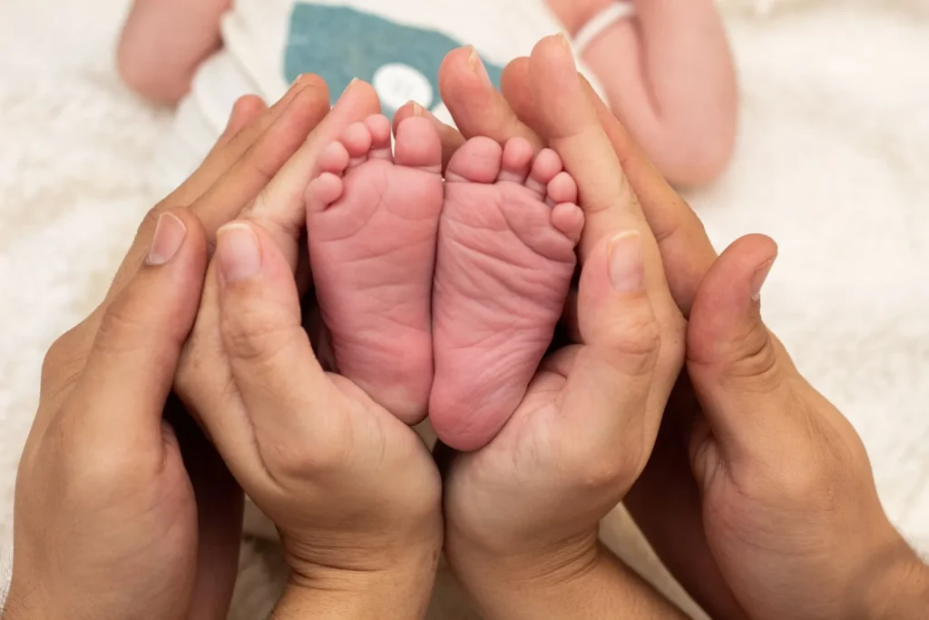Pies de un recién nacido sostenidos por las manos de sus padres, custodia de un lactante