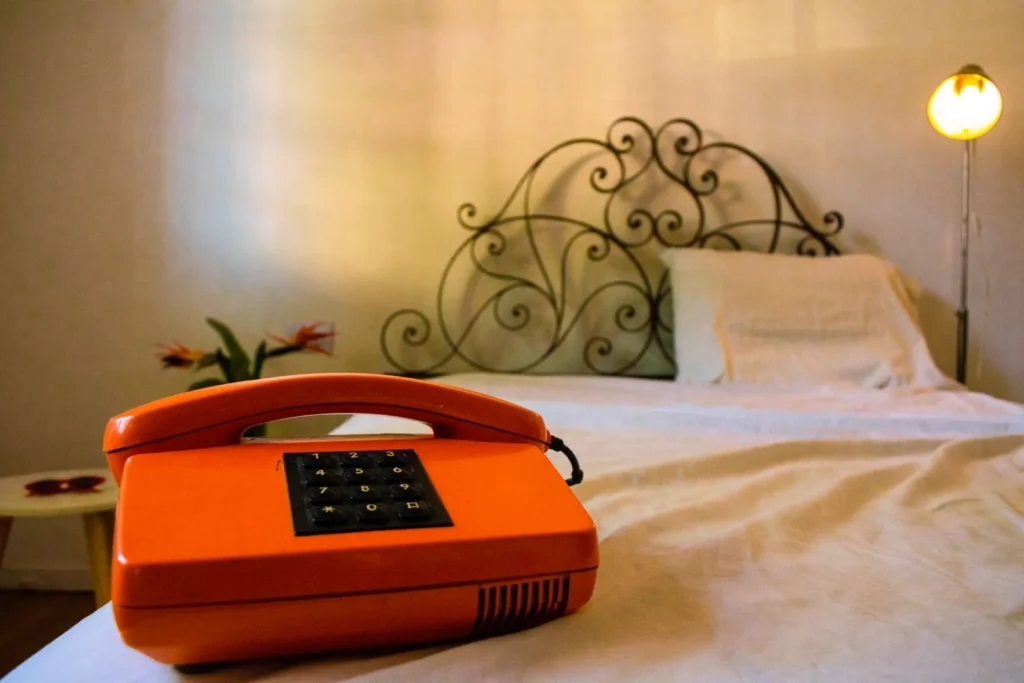 Teléfono naranja retro sobre una cama deshecha, infidelidad en el divorcio